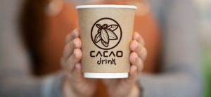 Barista sosteniendo un vaso de café de papel con el logo de Cacao Drink